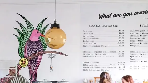 The café's pink bird mural beside the hand-lettered drinks menu board.