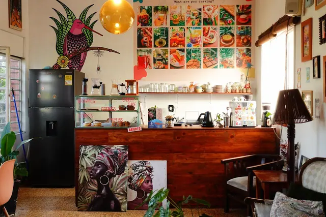 The coffee shop: wooden counter, pastry case, the pink bird mural and the wall of food photos.