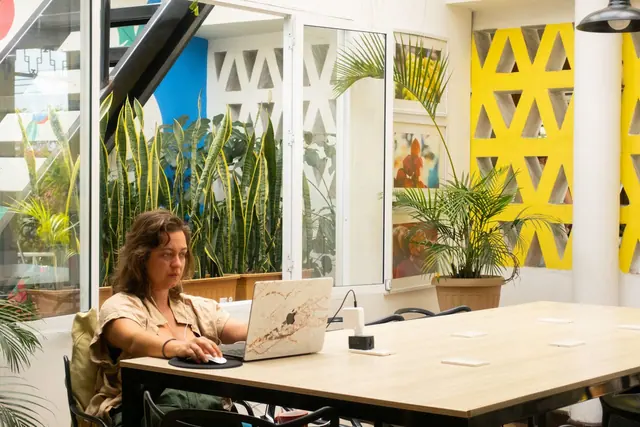 A guest working on a laptop at the long coworking table beside yellow and white breeze-block walls.