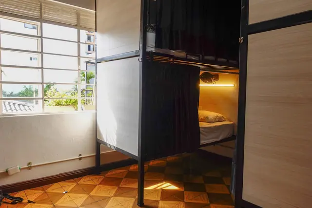 A curtained bunk with its own reading light, beside a sunny window and patterned tile floor.