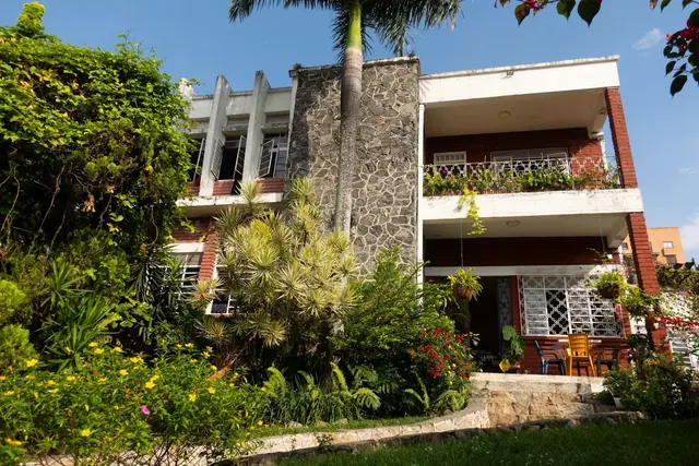 La Palmera's 1960s house: white balconies, red brick, a stone-clad wall and a tall palm above the front garden.