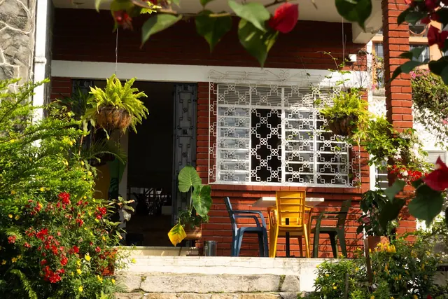 The front porch of the brick house, framed by flowers and hanging plants.
