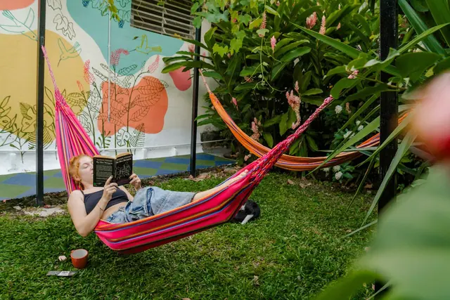 A guest reading in a pink hammock on the garden lawn, beside a leafy mural.