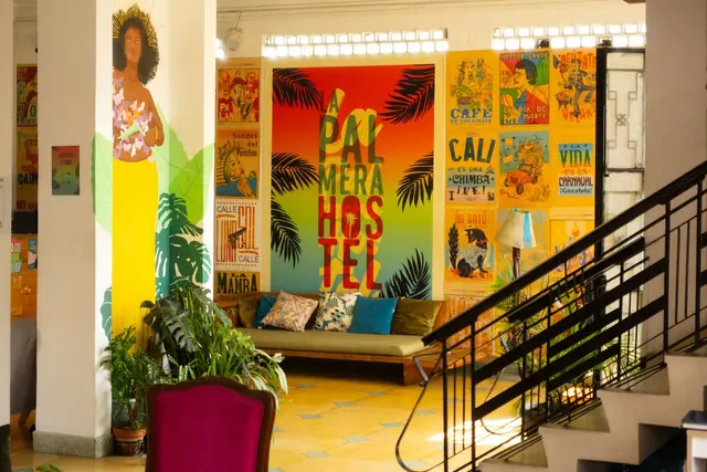 The lobby: the rainbow 'La Palmera Hostel' mural, the poster wall, the staircase and a woman painted on a column.