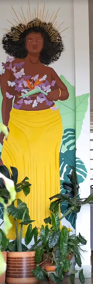 Mural of a woman crowned with golden rays, butterflies and a bird-of-paradise flower, surrounded by potted plants.