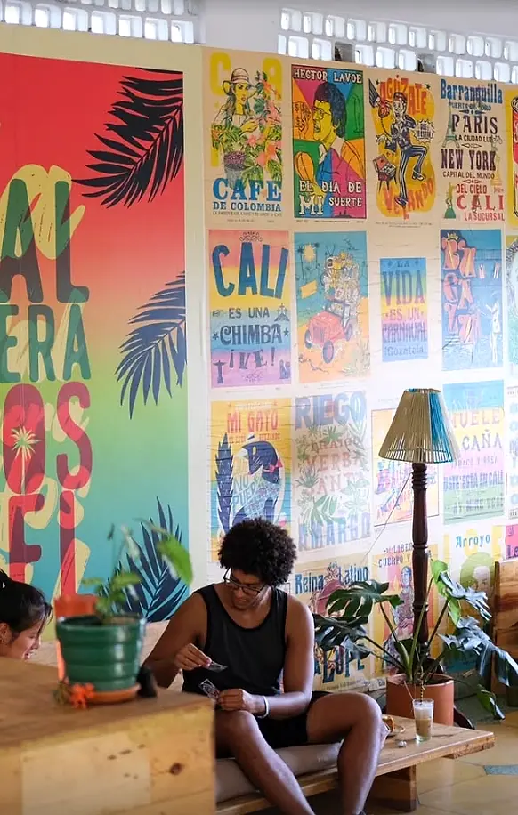 A guest playing cards on a daybed in front of the lobby's wall of colourful Cali posters and the big La Palmera mural.