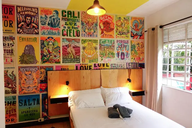 A bright private room with a double bed under a wall of Cali posters.